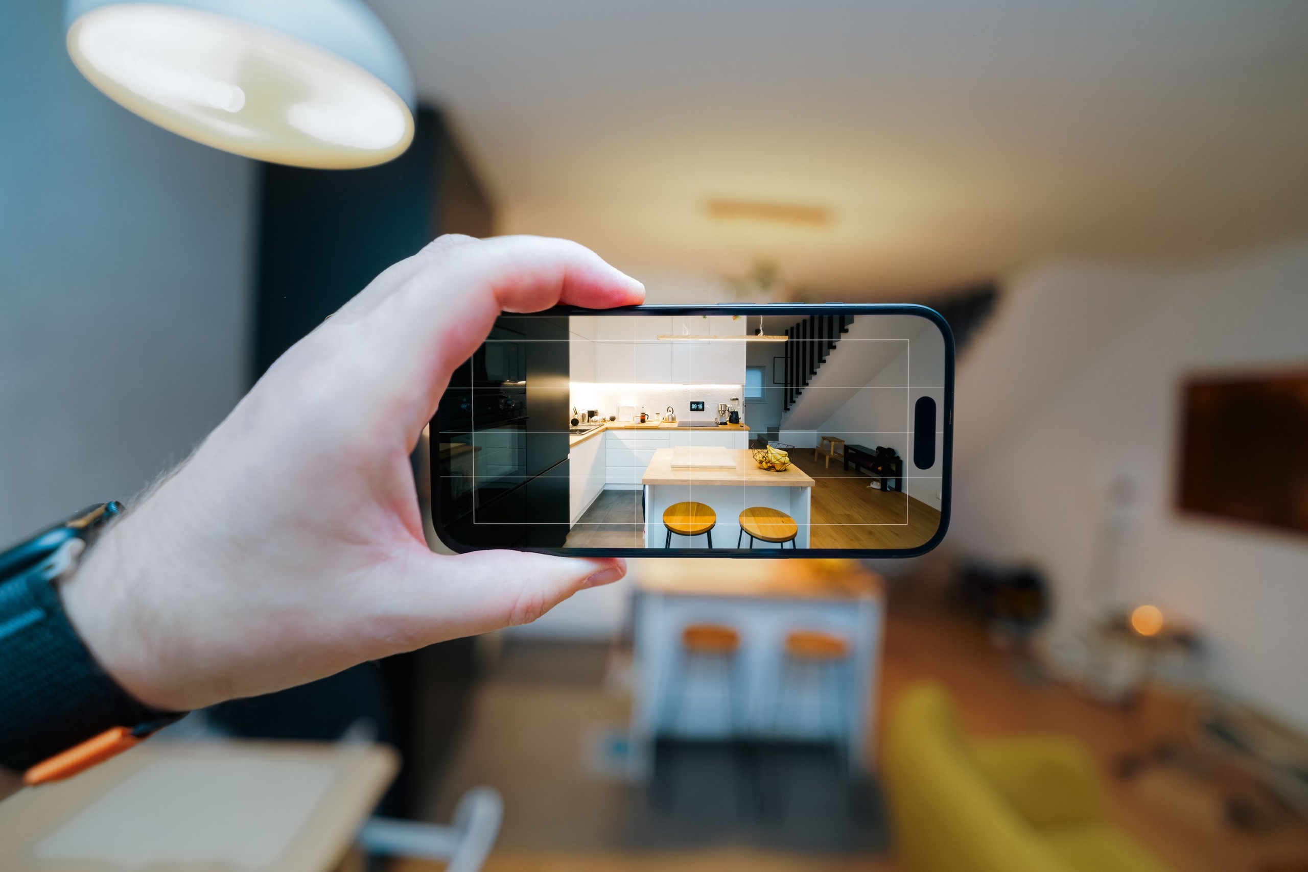 A smartphone in focus capturing a modern kitchen interior, showcasing real estate potential