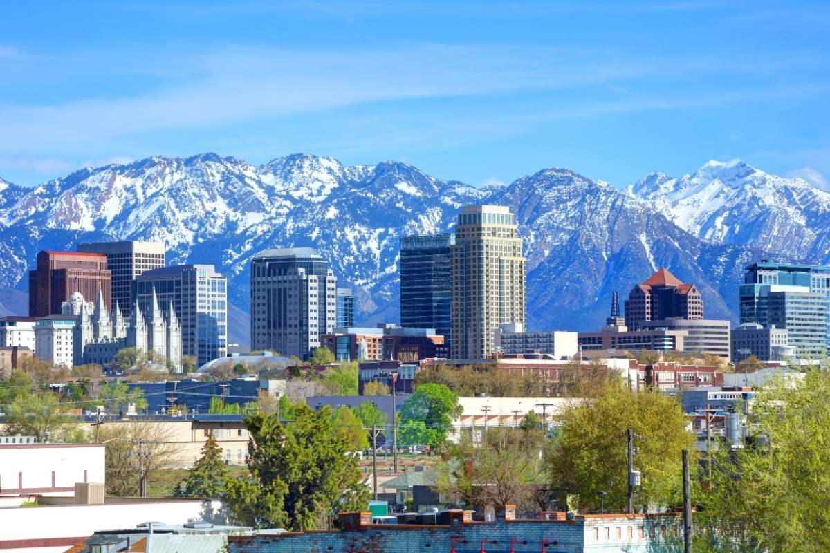 Downtown Salt Lake City skyline with modern buildings in front of snow-capped Utah mountains under a blue sky, highlighting vibrant commercial property management opportunities. Commercial property buildings in downtown Salt Lake City, Utah managed by Advanced Solutions Property Management.