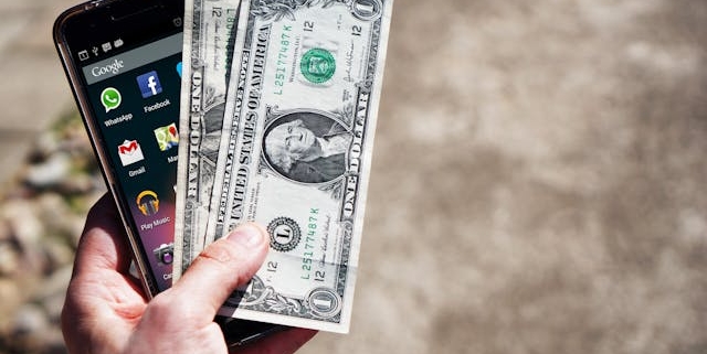 a-hand-holding-a-smartphone-and-two-one-dollar-bills a-hand-holding-a-smartphone-and-two-one-dollar-bills
