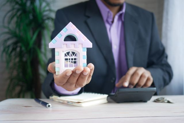 person holding a miniature house with a calculator