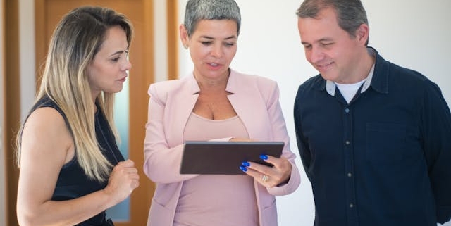 woman-in-pink-suit-showing-tablet-to-smiling-couple-in-bright-hallway woman-in-pink-suit-showing-tablet-to-smiling-couple-in-bright-hallway
